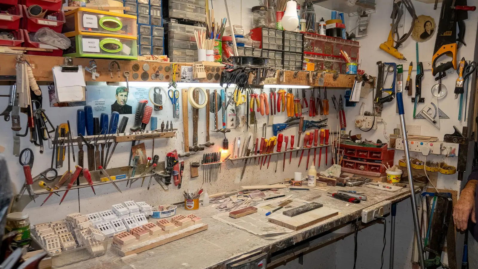 A workshop wall lined with hand tools above a busy workbench.