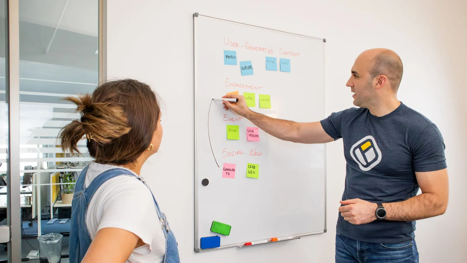 Two coworkers reviewing sticky notes on a whiteboard.